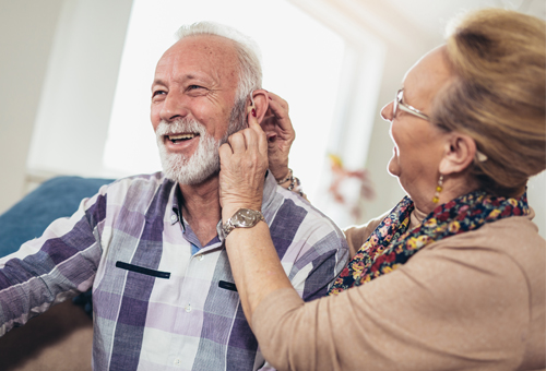 Woman placing a hearing aid in a mans ear.